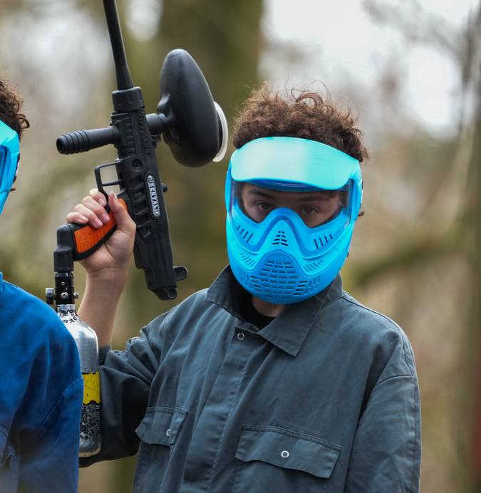 Gros plan sur un joueur de paintball portant un masque de protection turquoise et tenant son marqueur, lors d'une fête d'anniversaire paintball à La Hulpe