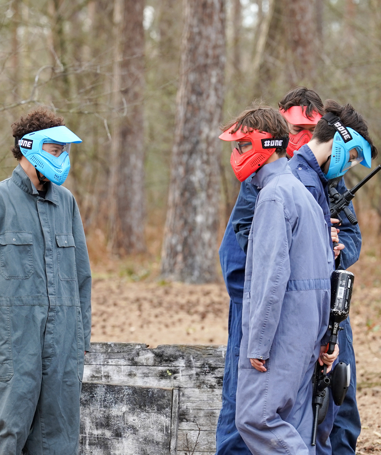 Groupe de joueurs en combinaisons et masques de protection colorés debout sur le terrain de paintball en forêt lors d'un anniversaire à Overijse