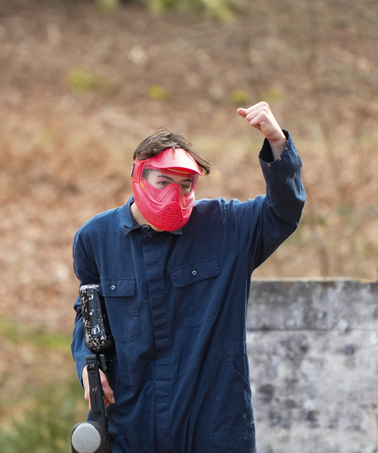 Joueur de paintball en combinaison bleue et masque rouge levant le bras en signe de victoire lors d'une fête d'anniversaire paintball à Rixensart