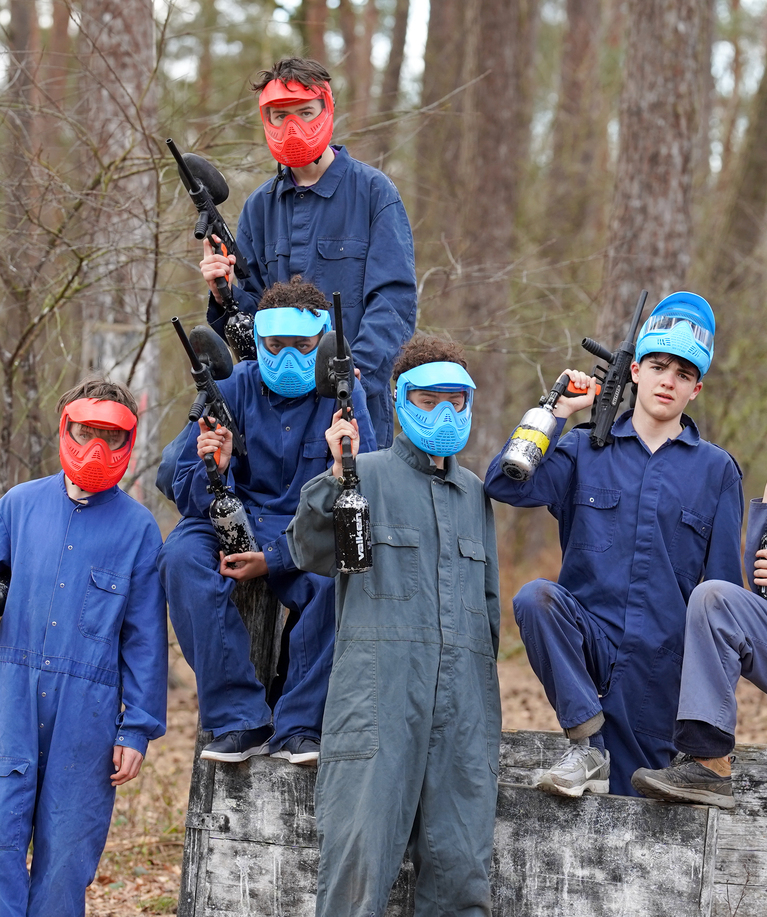 Groupe de joueurs de paintball en combinaisons bleues et masques de protection colorés posant ensemble en forêt lors d'une fête d'anniversaire paintball à Tervuren
